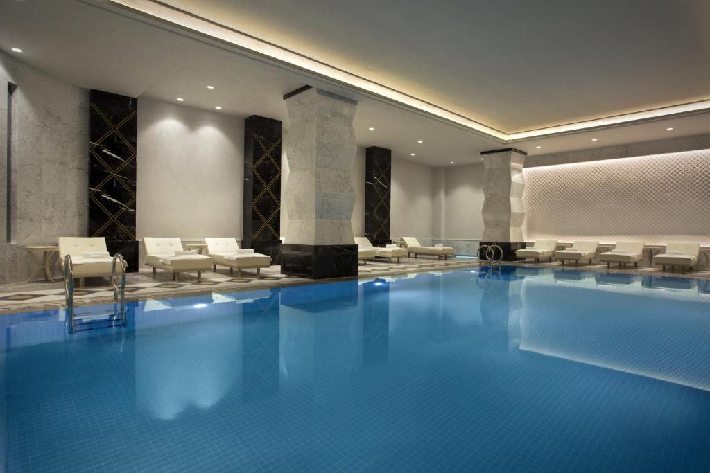 Lazzoni Hotel - a hotel lobby with a large swimming pool with white chairs at Lazzoni Hotel in Istanbul