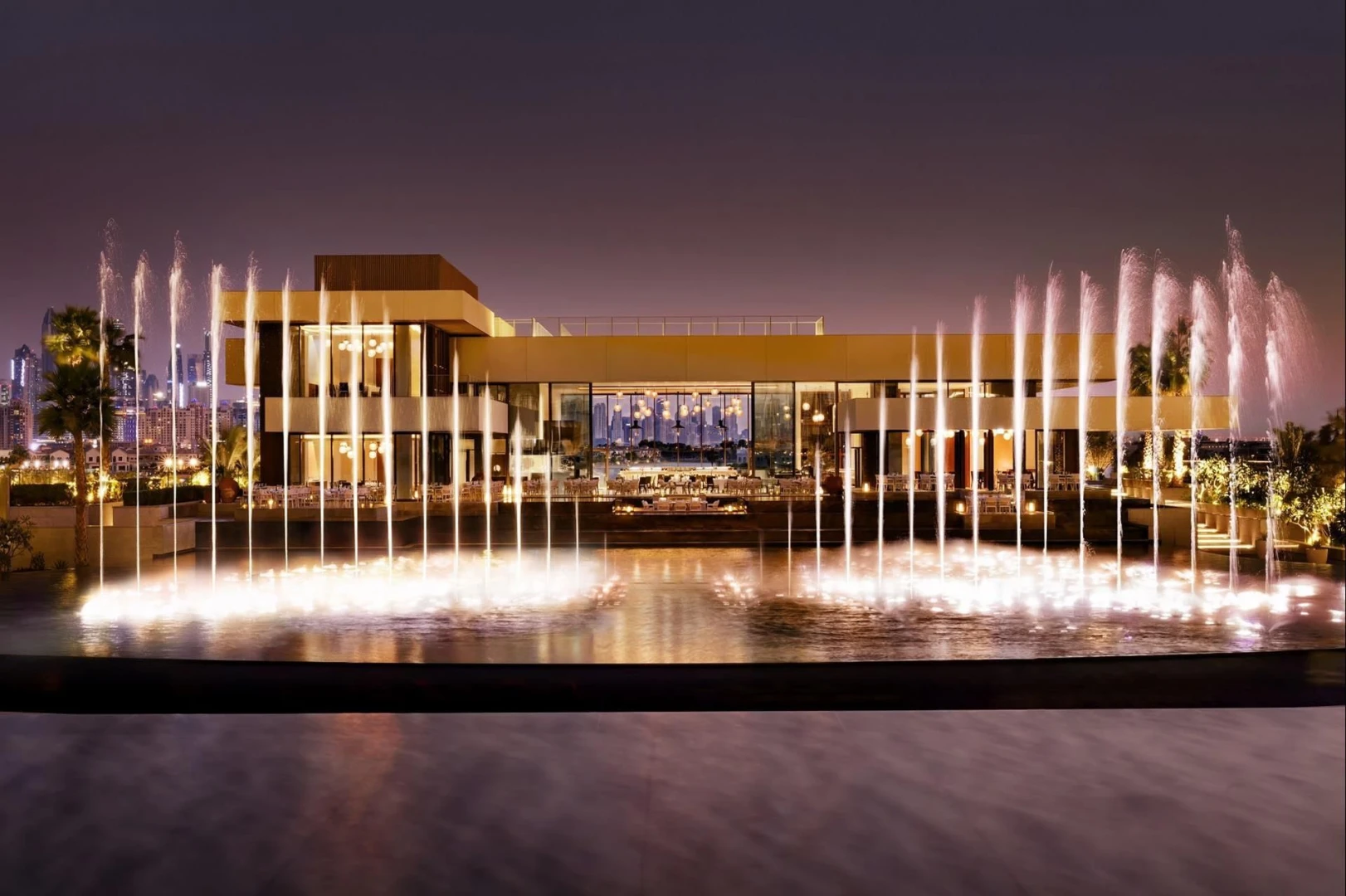 Atlantis The Royal Dubai illuminated with fountains at night.