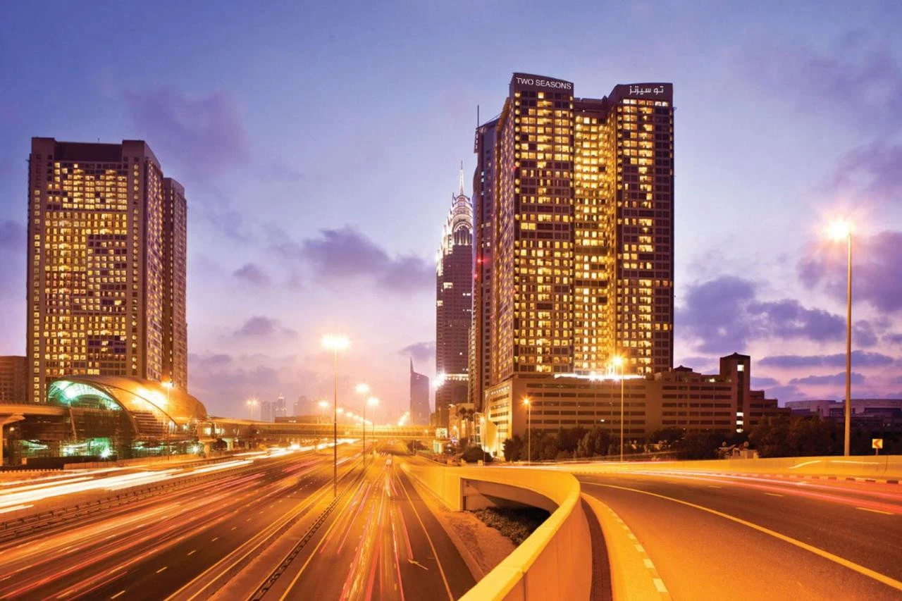 Two Seasons Hotel Dubai illuminated at dusk with busy highway view.