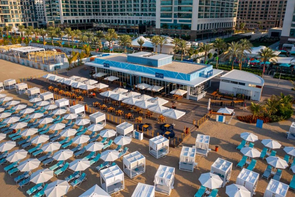 Beachfront view of Hilton Dubai Palm Jumeirah with umbrellas and loungers.