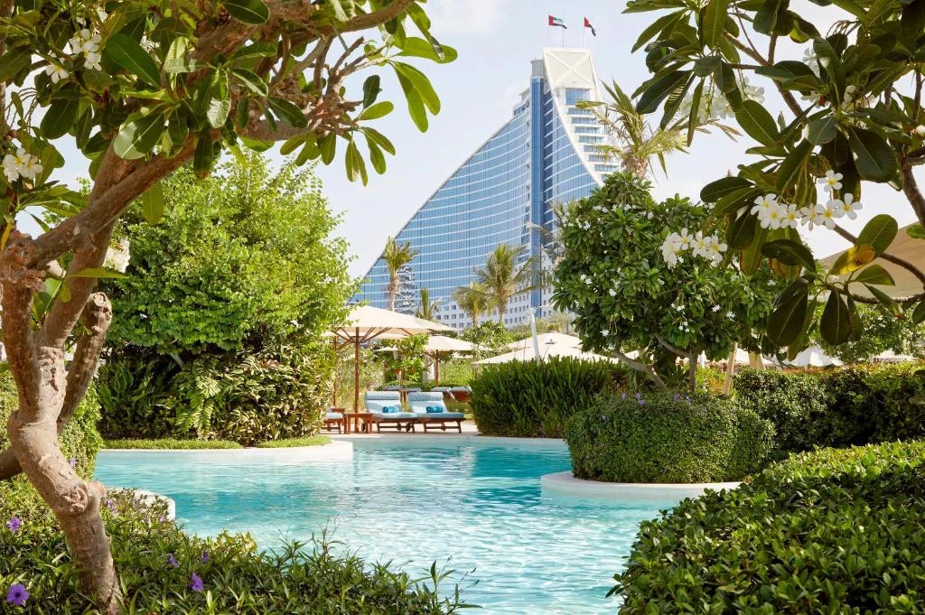 Jumeirah Beach Hotel poolside with lush greenery, Dubai skyline visible.