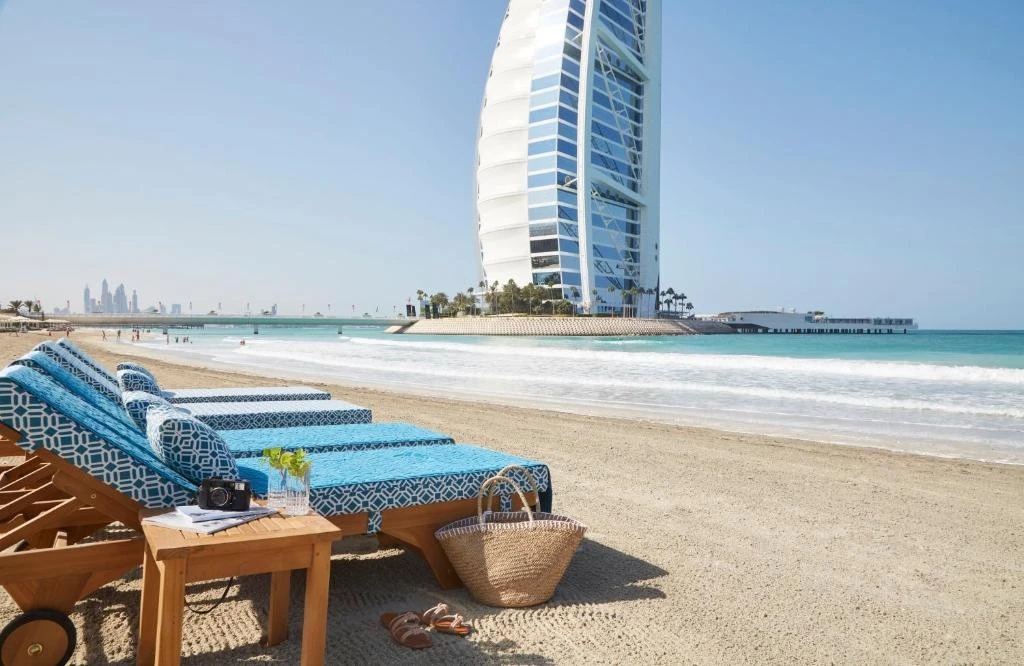 Jumeirah Beach Hotel beachfront with lounge chairs, Dubai skyline in background.