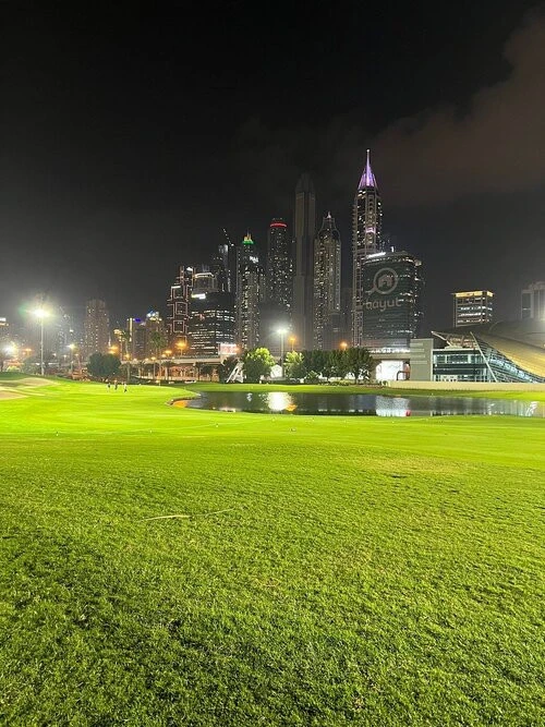 Night view of Emirates Golf Club with Dubai skyline in background.