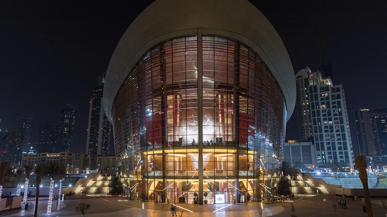 Dubai Opera illuminated at night with city skyline backdrop.