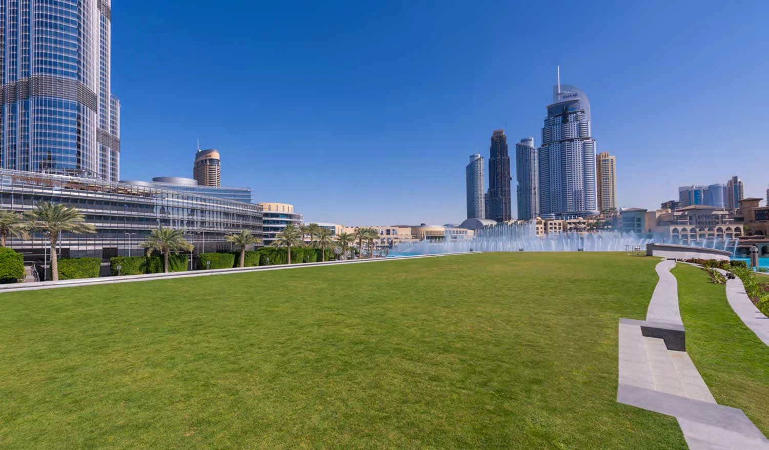 Dubai Opera lawn with skyscrapers and fountain in background.