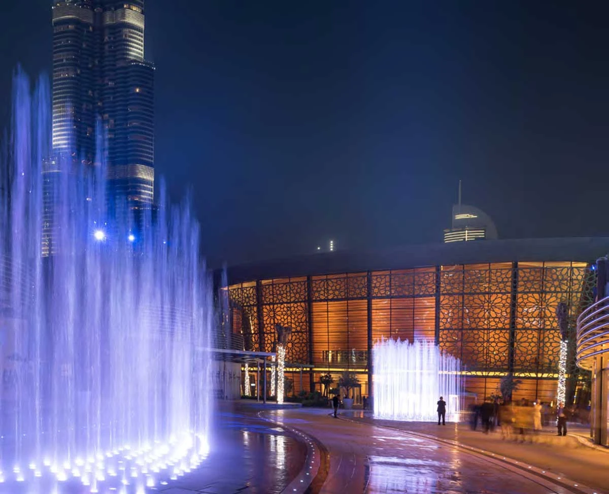 Dubai Opera illuminated at night with vibrant fountains.