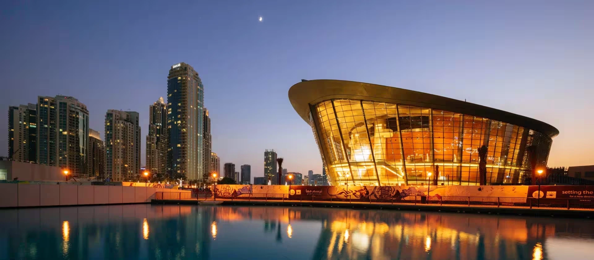 Dubai Opera illuminated at dusk, reflecting on nearby water.