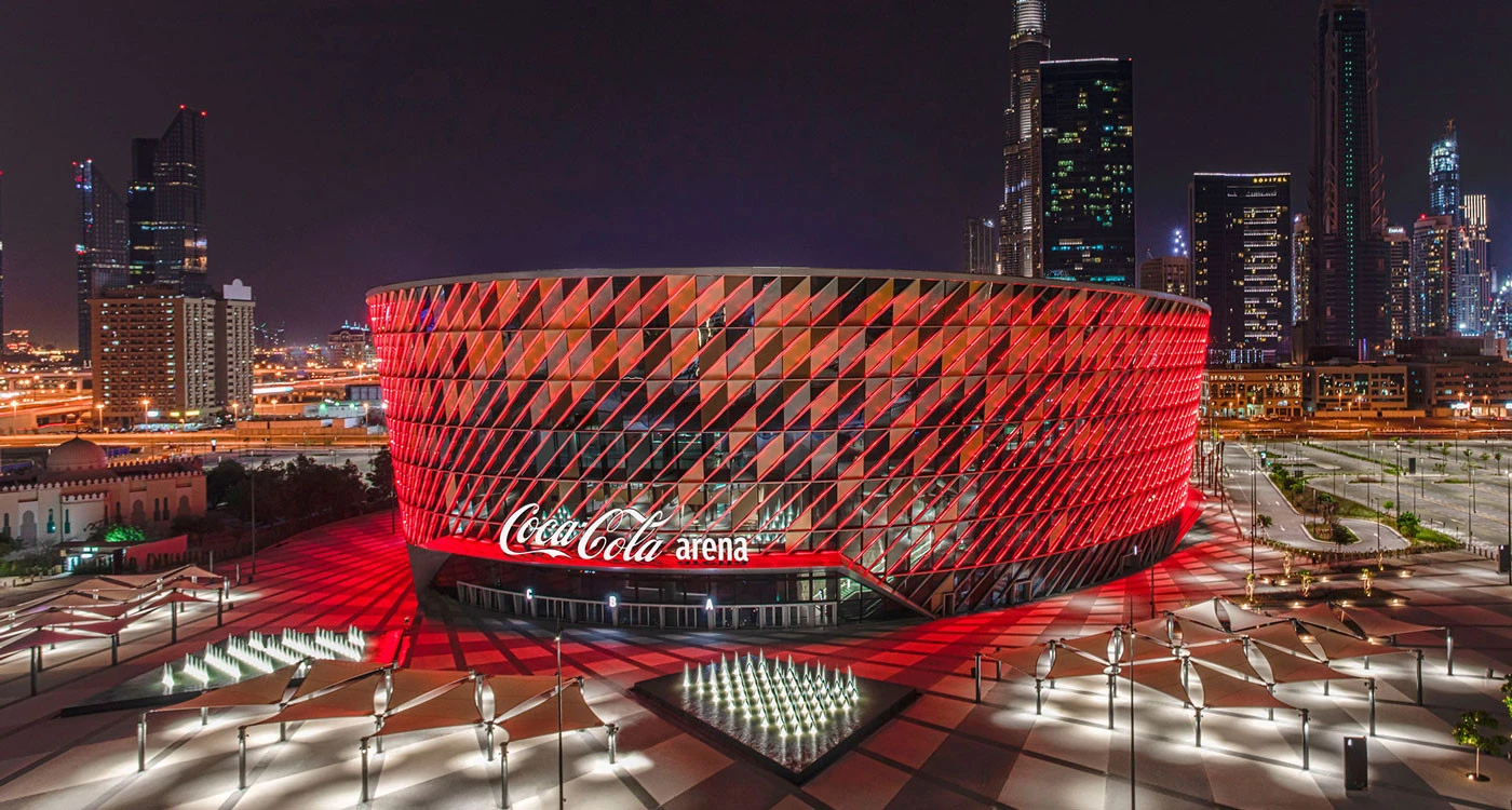 Coca-Cola Arena illuminated at night in Dubai cityscape.