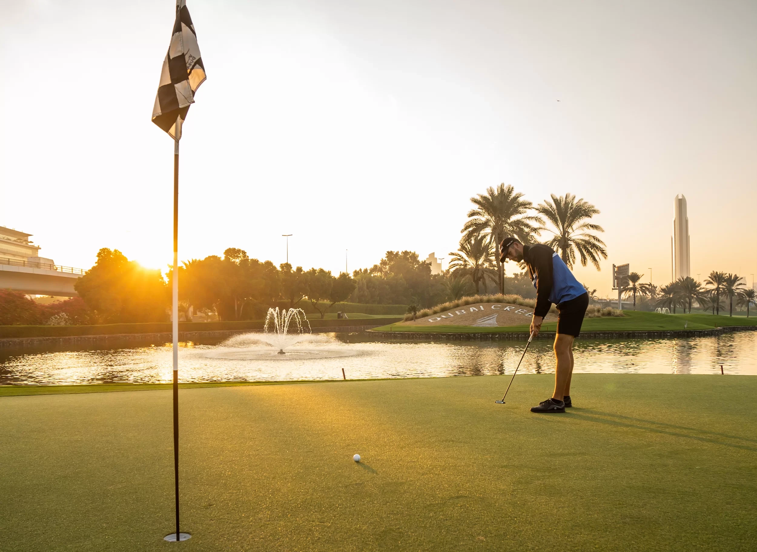 Golfer putting at Dubai Creek Golf & Yacht Club, sunset view.