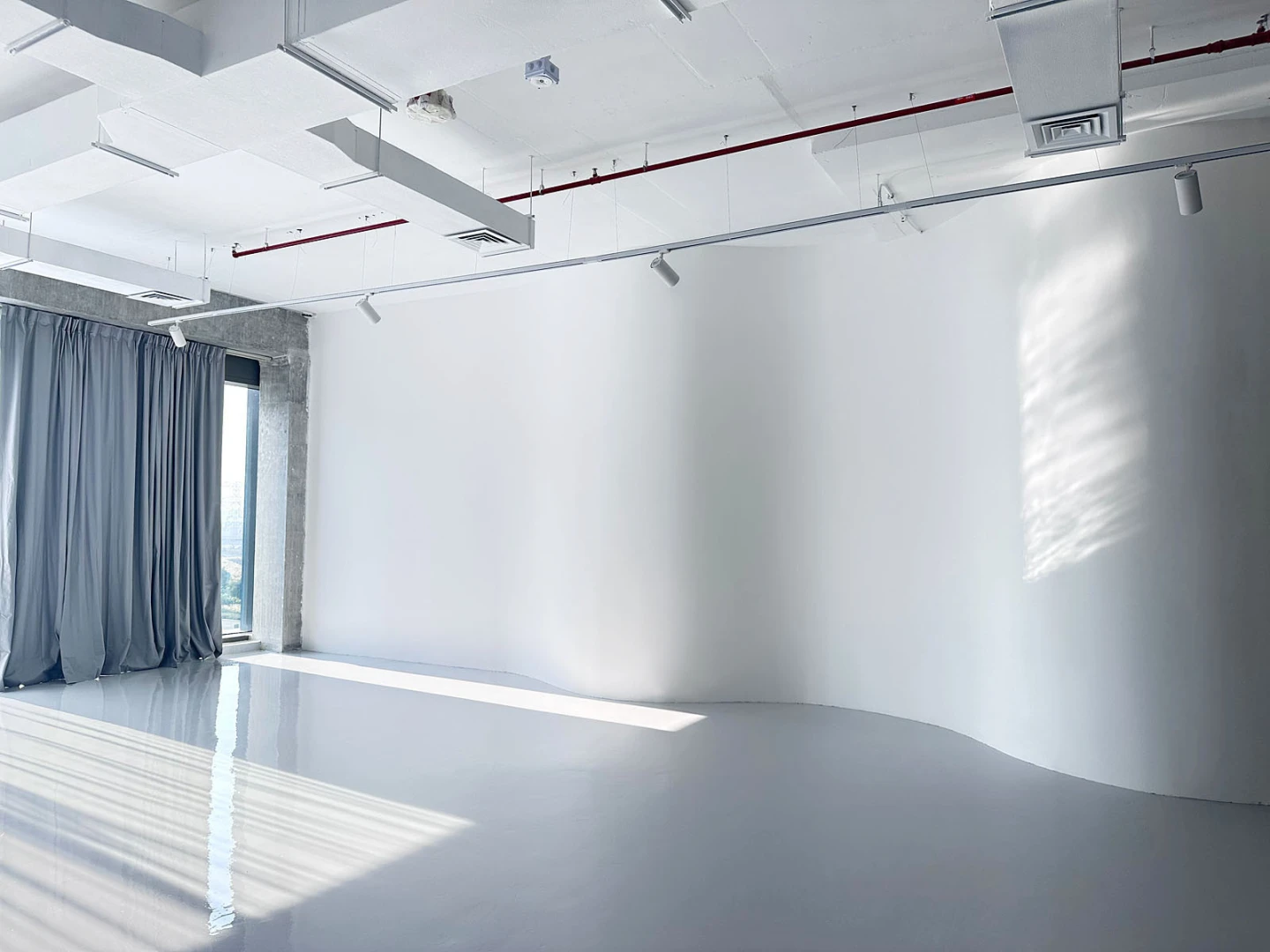 Spacious white studio with gray curtains at LUMA Studio, Dubai.