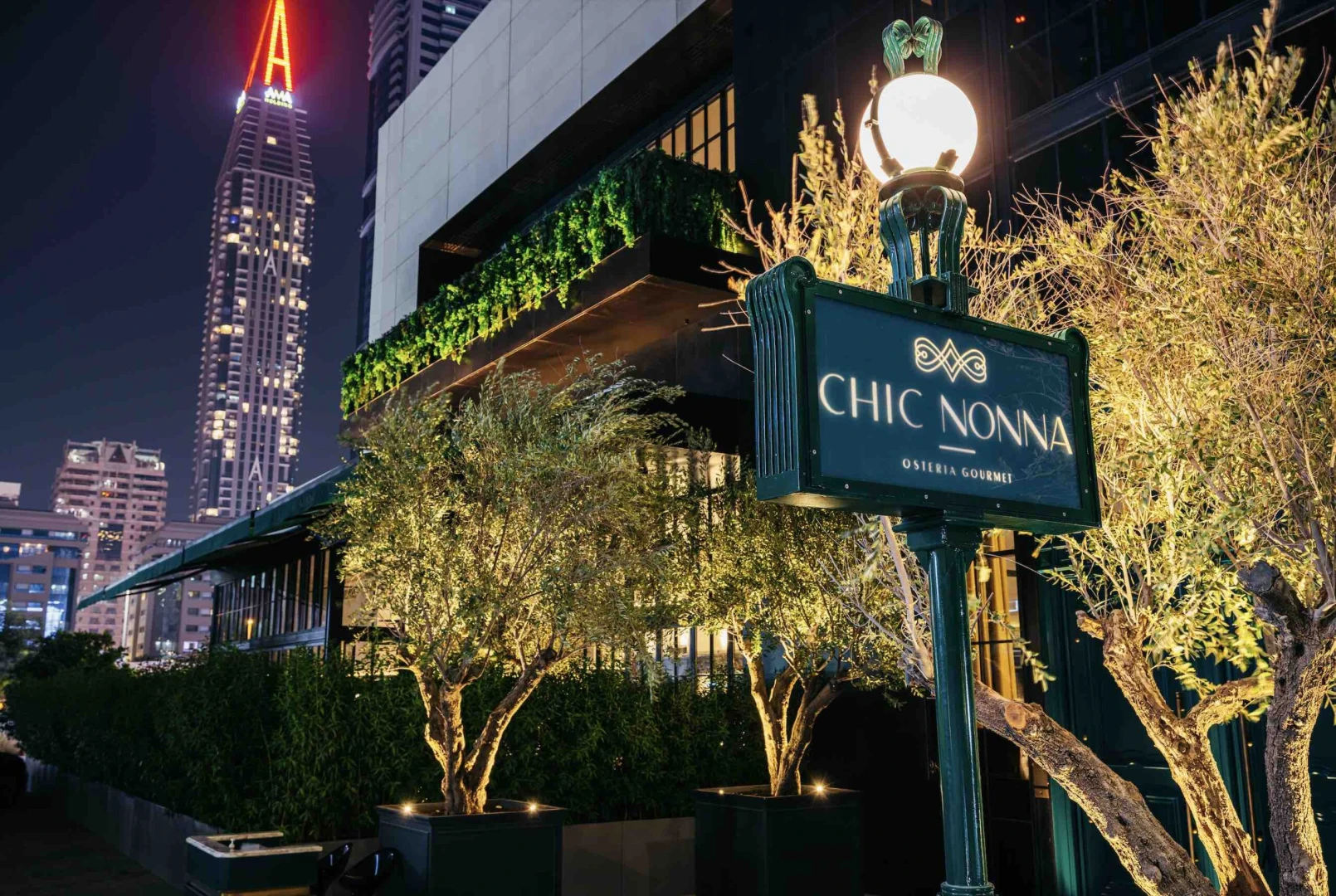 Chic Nonna Dubai entrance with illuminated trees and city skyline.