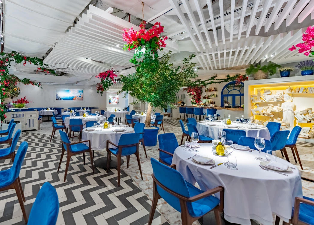 Opa Dubai dining room with blue chairs and vibrant floral arrangements.