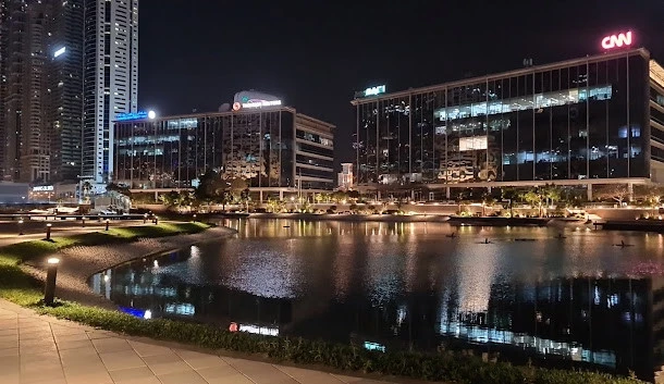 Dubai Media City Amphitheatre at night with illuminated buildings and lake.