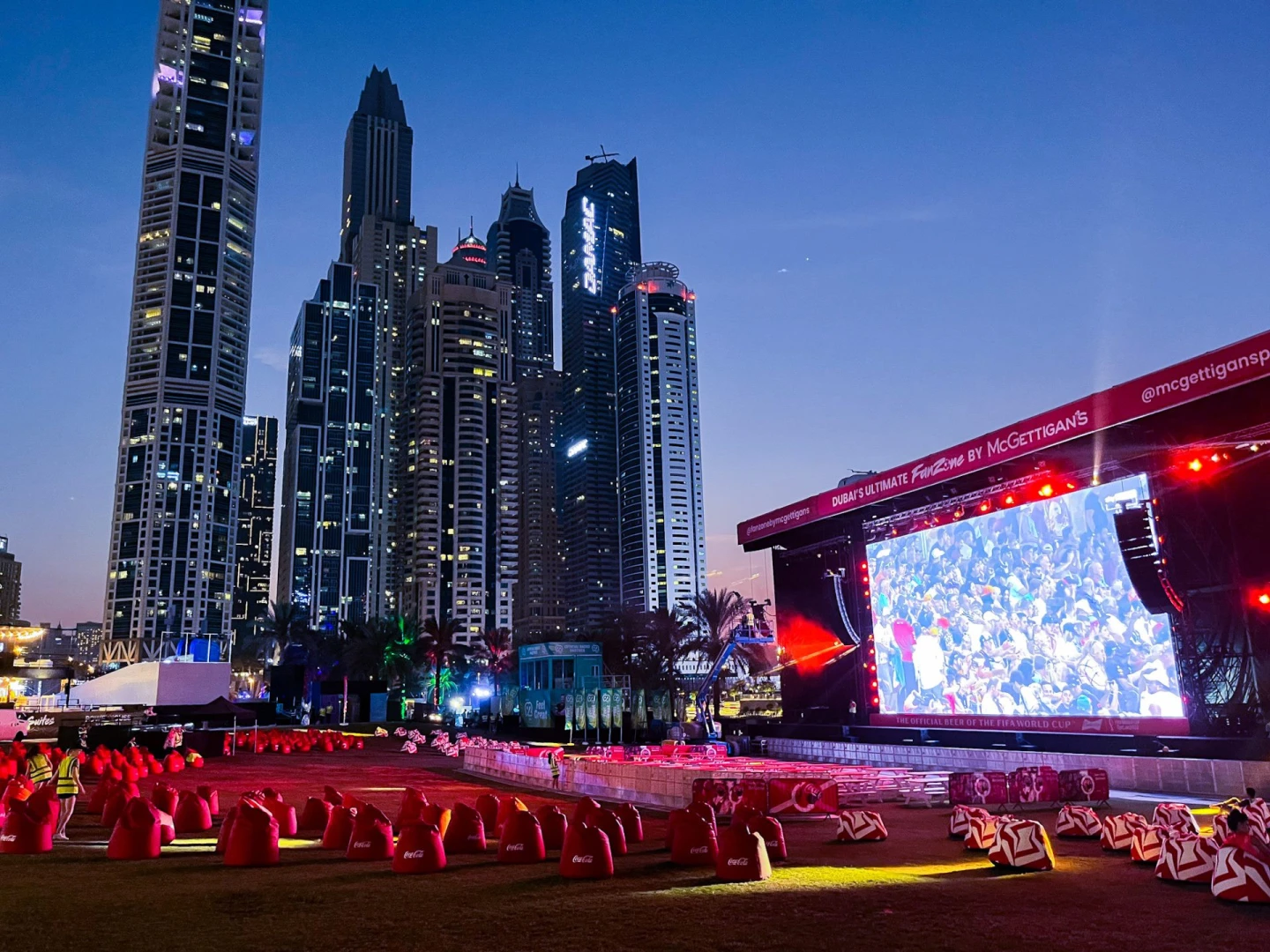 Dubai Media City Amphitheatre with skyscrapers and large outdoor screen at dusk.