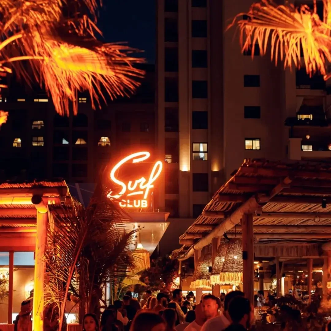 Surf Club Dubai at night with neon lights and palm trees.