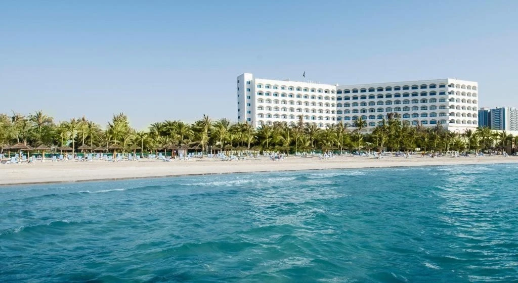Kempinski Hotel Ajman beachfront view with palm trees and ocean.
