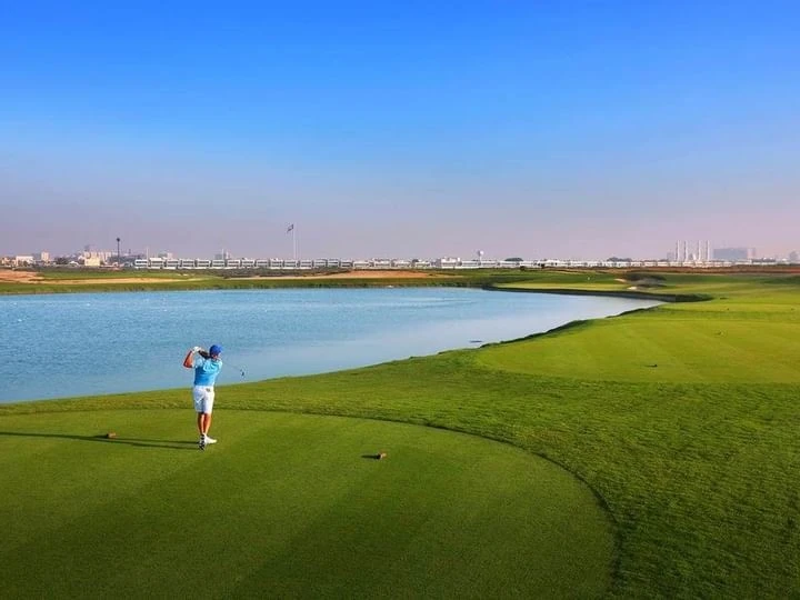 Golfer swings on lush course at Kempinski Hotel Ajman.
