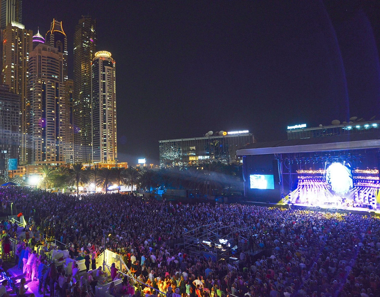 Crowd at Dubai Media City Amphitheatre with city skyline at night.