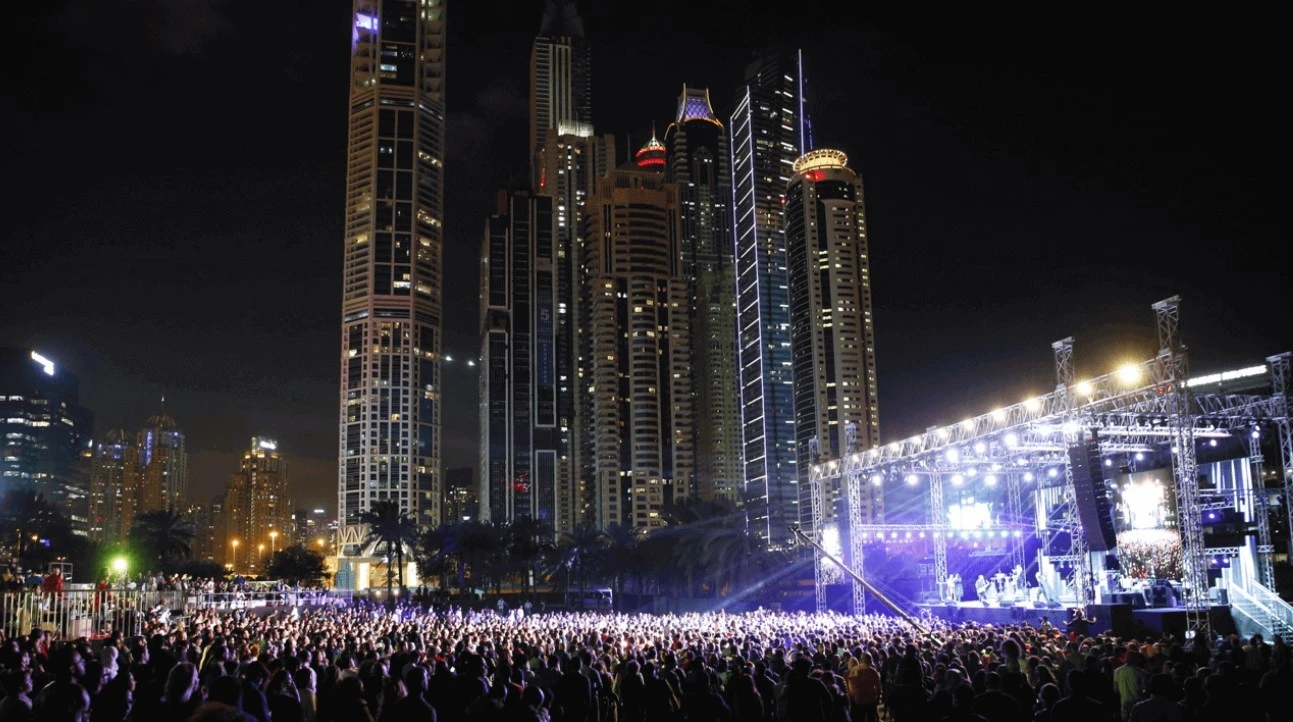 Crowd at Dubai Media City Amphitheatre with skyscrapers illuminated at night.