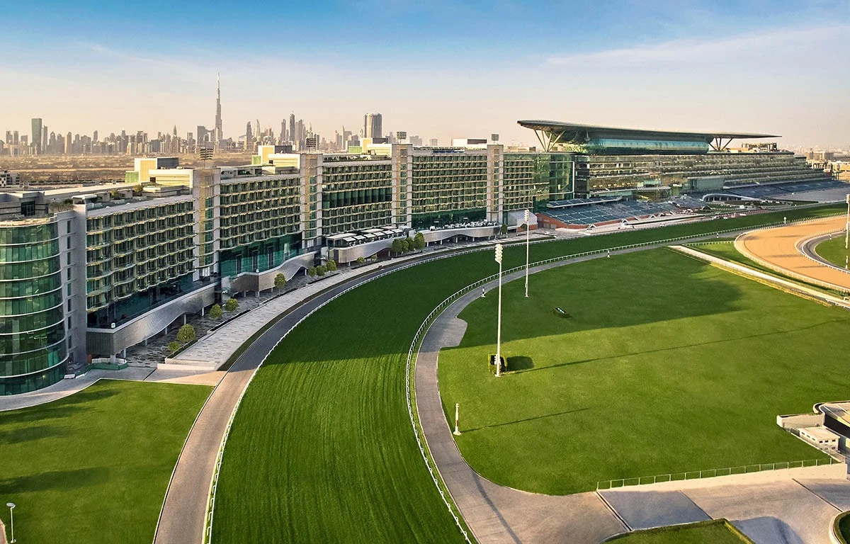 The Meydan Hotel exterior with racetrack, Dubai skyline in background.