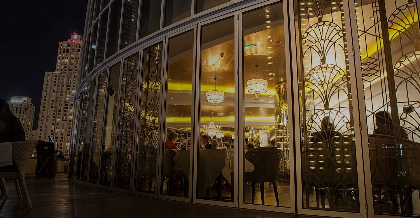Atelier M Dubai, elegant dining area with chandeliers at night.