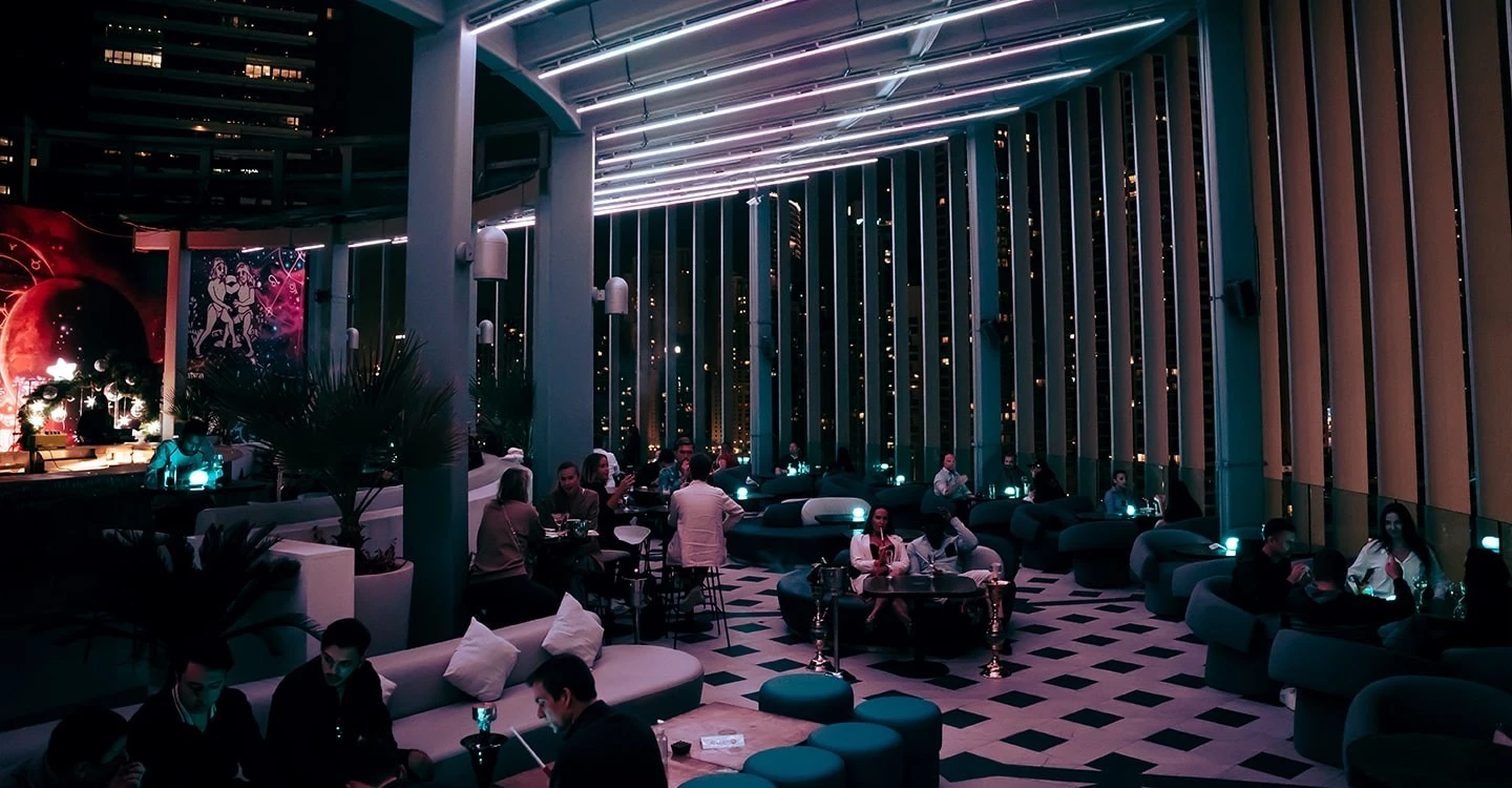 Atelier M rooftop lounge with patrons, Dubai skyline at night.