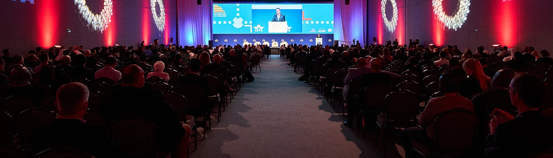 Packed audience at ADNEC Centre Abu Dhabi, blue-lit stage.