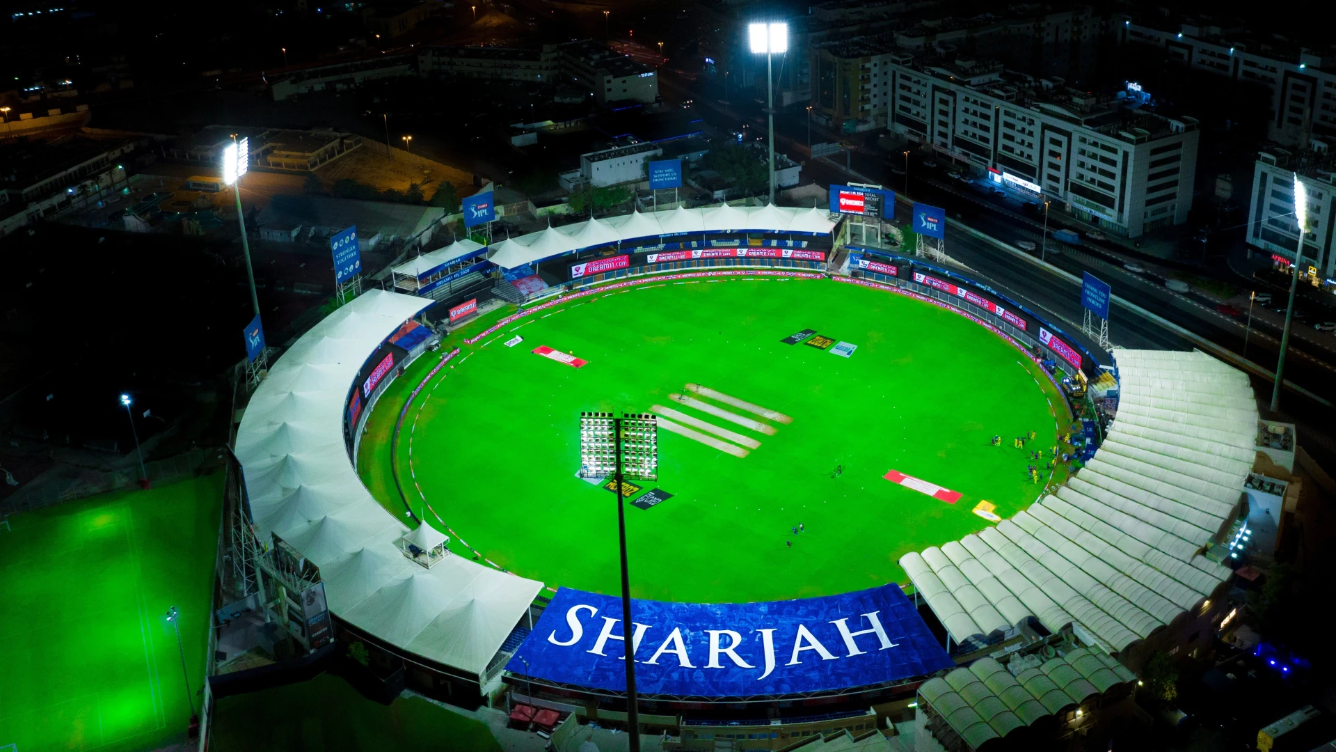 Aerial view of illuminated Sharjah Cricket Stadium at night.