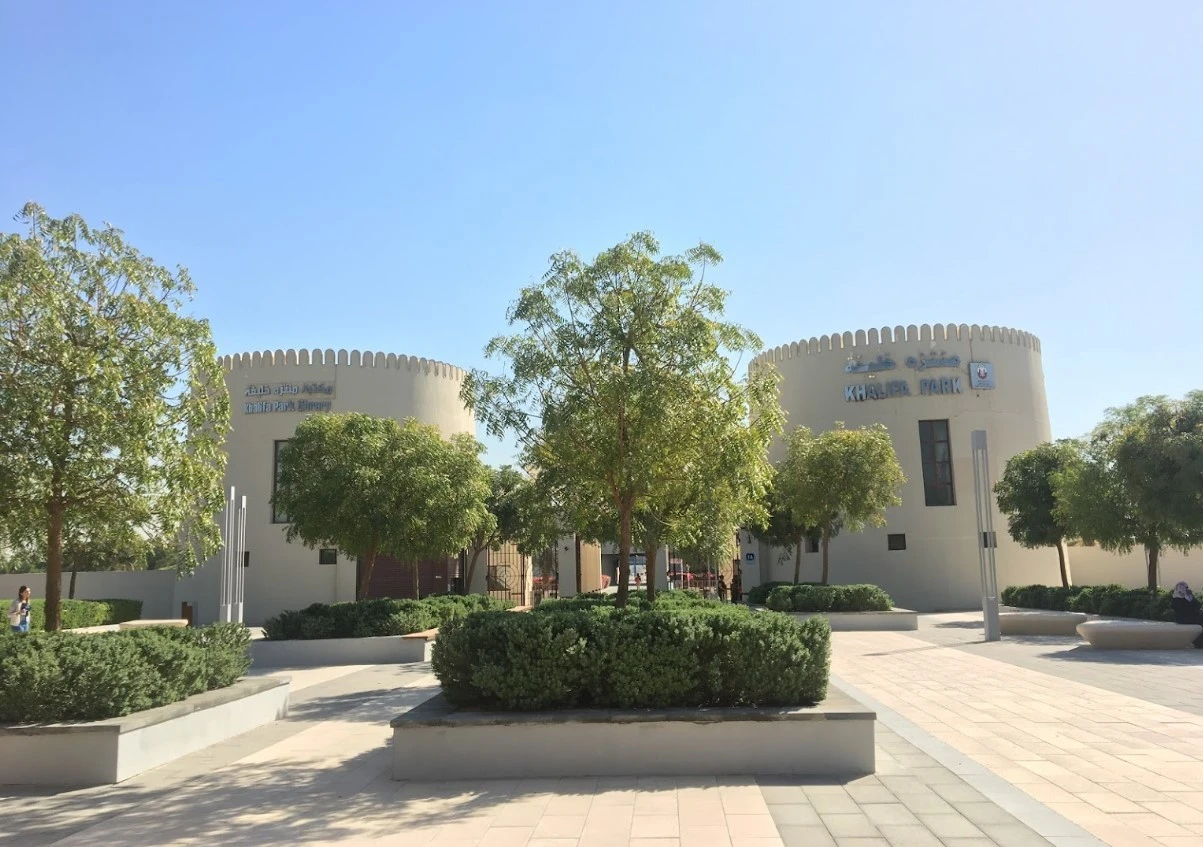 Khalifa Park Amphitheater entrance with trees, Abu Dhabi, sunny day.