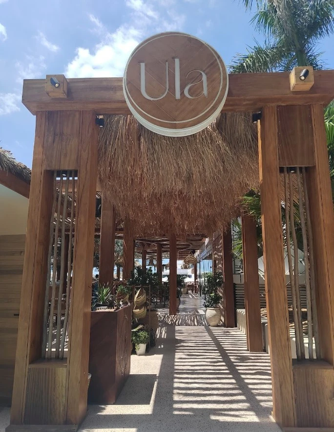 Entrance of Ula Dubai Beach Club with wooden decor and plants.