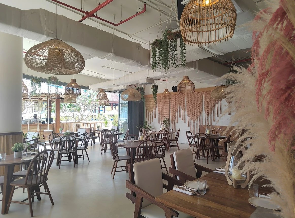 Ula Dubai Beach Club interior with wooden tables and wicker lamps.