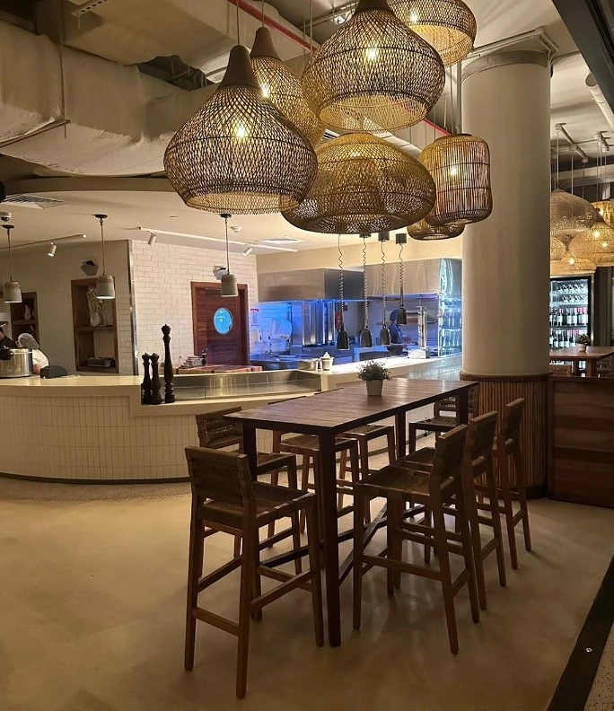 Ula Dubai Beach Club interior with wicker lights and wooden seating.