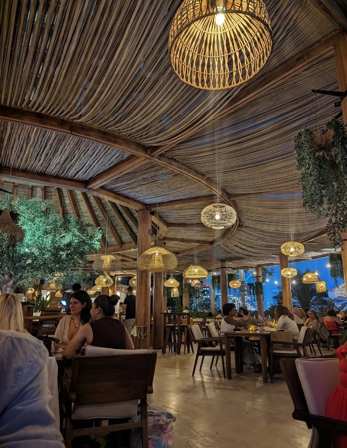 Ula Dubai Beach Club, cozy evening dining with woven lights and greenery.