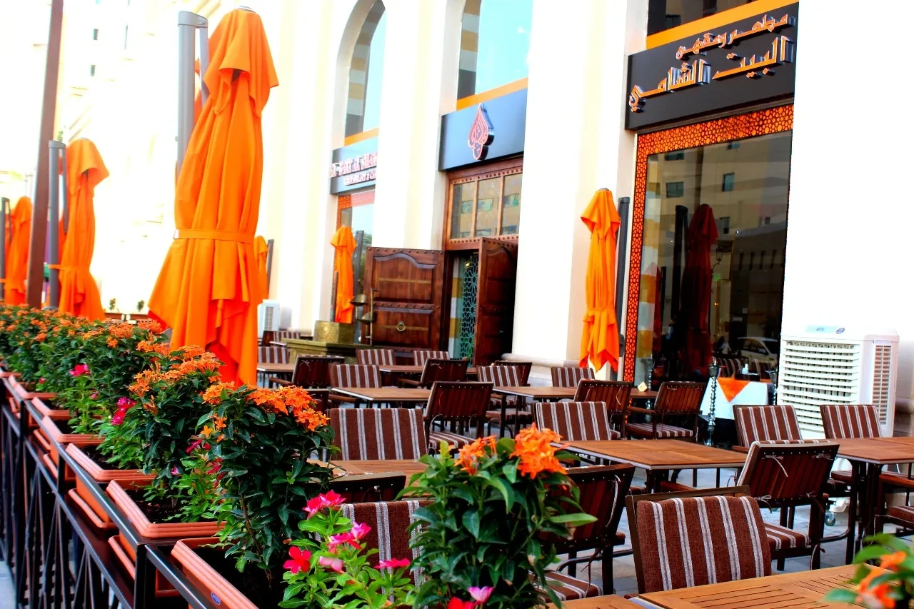 Outdoor seating at Al Bait Al Shami Restaurant, Dubai with orange umbrellas.