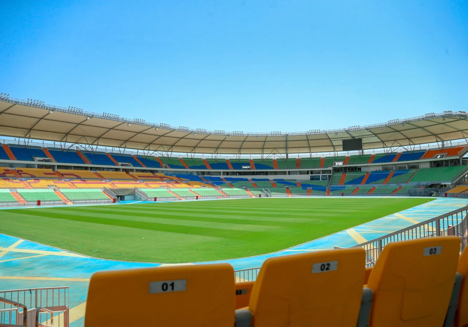 Empty Prince Abdullah Al Faisal Stadium, Jeddah, colorful seating, sunny day.
