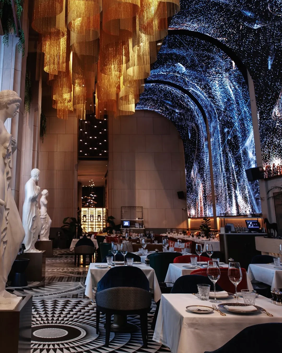 Elegant dining area at Zenon Restaurant Dubai with statues and chandeliers.