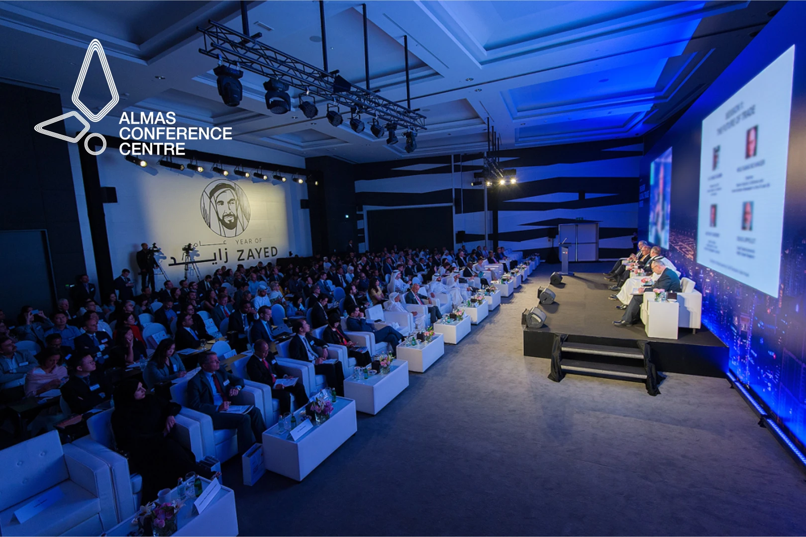 Conference at Almas Conference Centre, Dubai, with seated audience and speakers.