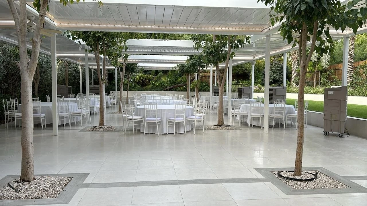 White tables under pergola with trees, The Farm, Dubai.