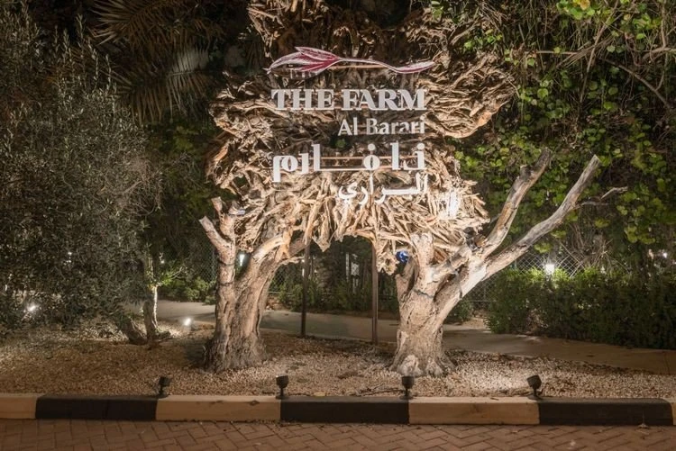 Entrance sign of The Farm Restaurant Al Barari, Dubai, surrounded by trees.