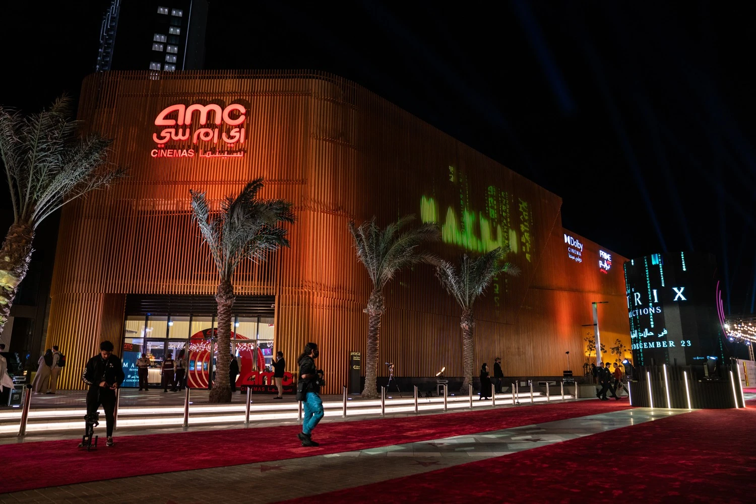 AMC Cinemas Ajdan Walk Al Khobar illuminated at night with palm trees.