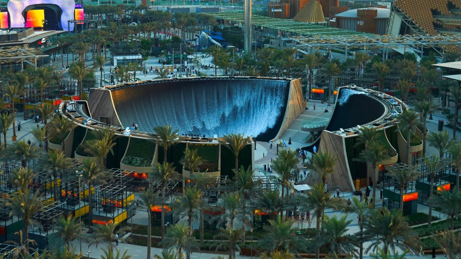 Surreal waterfall feature at Expo City Dubai with surrounding palm trees.