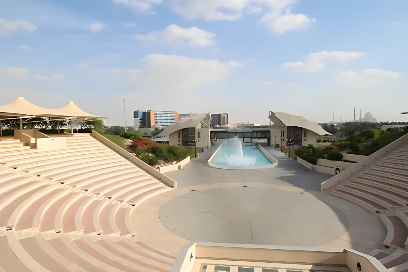 Khalifa Park Amphitheater with seating and fountain, Abu Dhabi skyline visible.
