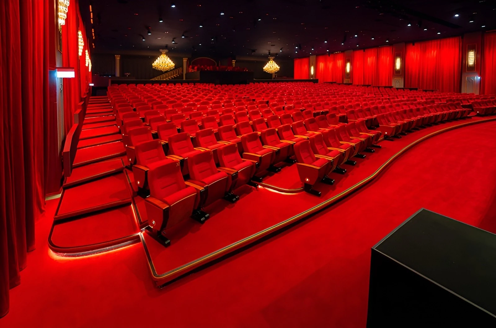 Red auditorium seating at U Venue Doha with chandeliers.
