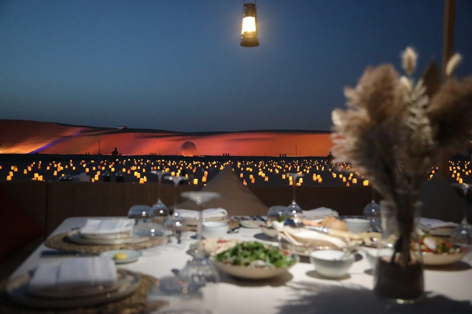 Elegant dining setup overlooking illuminated desert at The Outpost Al Barari, Doha, QATAR.