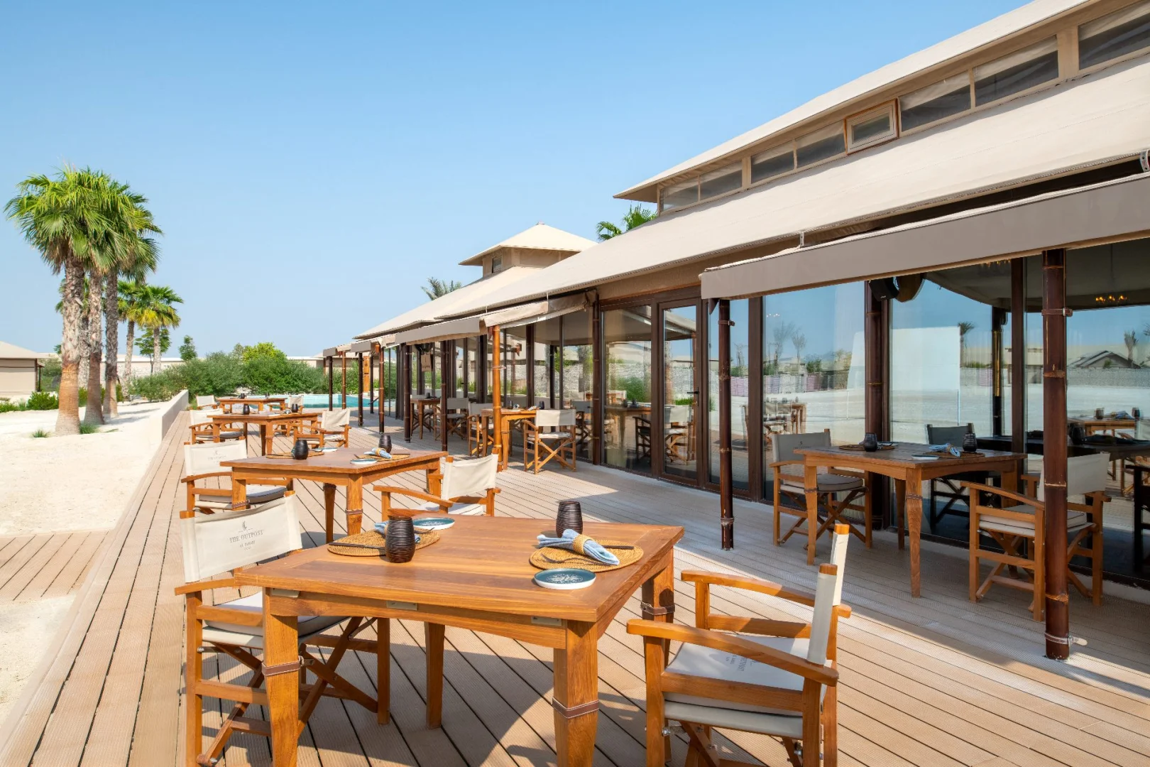 Outdoor dining area with wooden tables at The Outpost Al Barari, Doha, QATAR